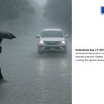 Man with an umbrella walks through a flooded street during heavy rainfall in Telangana, as a white SUV drives through the downpour
